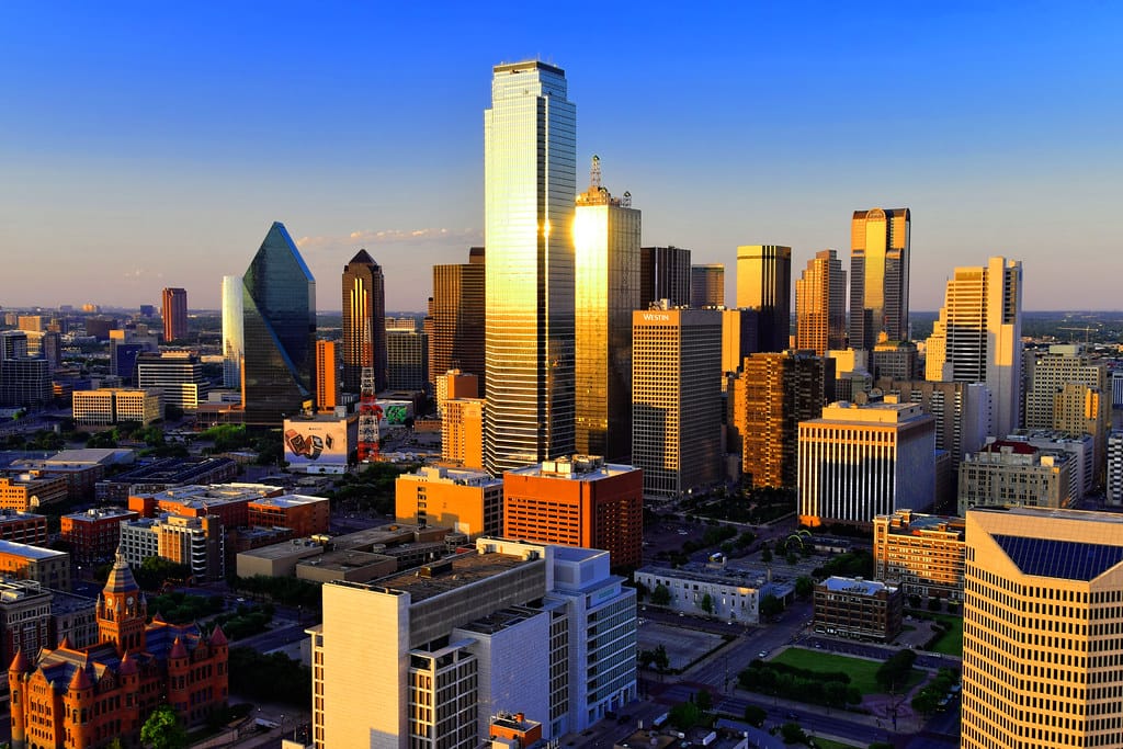 Downtown Dallas skyline at sunset, with golden light reflecting off glass skyscrapers.