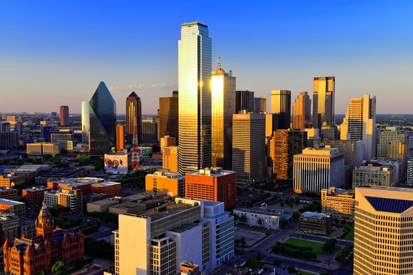 Downtown Dallas skyline at sunset, with golden light reflecting off glass skyscrapers.