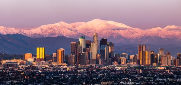 Los Angeles skyline at sunset with snow-capped mountains glowing in the background.